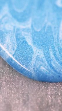 Dikey video. Renkli damlalar. Soyut mürekkep. Mavi dalga üzerindeki beyaz şeritler sıvı okyanus boyası dokusu parıldayan gri ahşap simler bokeh çözünmüş..