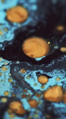 Dikey video. Yağ sızıntısı. Parıldayan kabarcıklar. Mürekkep karışımı. Odaklanmamış mavi altın rengi parlak yuvarlak damlacıklar desen boya akışı soyut sanat arkaplanı.