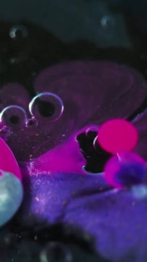 Dikey video. Boya baloncukları. Yağlı sıvı sıçraması. Odaklanmamış neon mavisi akrilik mürekkep boyalı su karışımı simli jel damlacıkları koyu siyah soyut sanat arka planında yüzüyor..