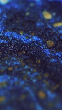 Dikey video. Islak sim dokusu. Boya akışı. Odaklanamayan mavi altın rengi, parlak parçacıklar akrilik mürekkep dalgası hareketini koyu soyut sanat arka planında.