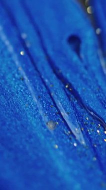 Dikey video. Parlak sıvı damlası. Boya dökülmüş. Odaklanmamış mavi altın rengi parıldayan desen mürekkebi emülsiyon akışı hareketini soyut sanat arkaplanı.