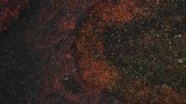 Islak sim sıçraması. Işıldayan doku. Odaklanmamış bronz, kırmızı, altın sarısı, parlak toz parçacıkları jel boya akışı koyu, soyut sanat arka planı..