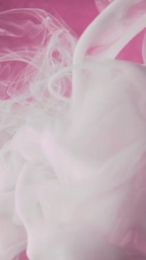Dikey video. Sigara sanatı. Boya suyu girdabı. Mürekkep bulutu. Beyaz ipek akrilik sıvı akış dokusu çözünmüş pembe renk tahıl özeti arka planında sis hareketi.
