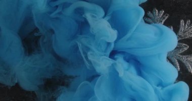 Noel arkaplanı. Kar tanesi mürekkebi. Mavi renkli boya. Duman bulutu yayılıyor. Siyah üzerine ışıl ışıl gümüş aksesuar..