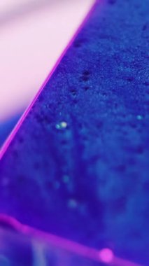 Dikey video. Buz küpü. Donmuş boya. Odaklanmamış mavi pembe neon yüzler geometrik şekil ıslak yüzey üzerinde parıldayan sıvı soğuk prizma hareket soyut sanat arka planı.