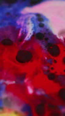 Dikey video. Boya karışımı. Mürekkep karışımı. Odaklanmamış kırmızı mavi pembe pembe parıldayan yağ sıvısı lekeleri parlak parlak, soyut sanat arka planında yüzüyor..