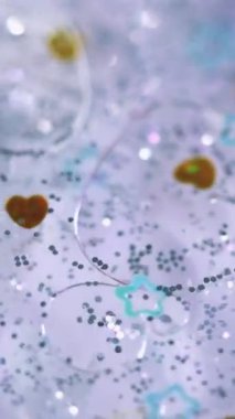 Dikey video. Yağ damlası sıvısı. Parıldayan şekiller. Disko ışığı. Odaklanmamış mavi, mor, altın, gümüş rengi, parlak pullar, kalp, yıldız parçacıkları soyut sanat arka planında yüzerler..