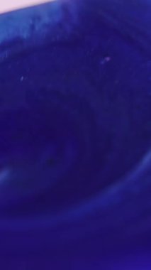 Dikey video. Boya damlası. Parlak kare. Odaklanmamış mavi beyaz renkli sıvı jet geometrik şekilli ışıltılı küp ıslak mürekkep akışı hareketini soyut sanat arka planına döküyor.