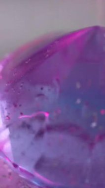 Dikey video. Kristal prizma. Elmas değerli taş. Odaklanamayan mor renkli, yanardöner lüks mücevher su damlaları parlak taş parçacıkları soyut sanat arka planını yansıtıyor..