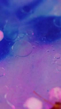 Dikey video. Köpüklü sim boyası. Uçan çiçekler. Odaklanmamış pembe renk yarı şeffaf yağ damlaları parıldayan jel yaprakları soyut sanat arkaplanı..