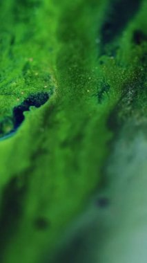 Dikey video. Mürekkep döküldü. Parlak sıvı damlası. Odaklanmamış yeşil sarı beyaz renk parıldayan ıslak boya karışımı hareket bokeh hafif doku soyut sanat arkaplan.