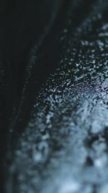 Dikey video. Parlak sıvı dökülmüş. Parlak mürekkep karışımı. Bulanık siyah gümüş rengi metalik parıldayan kum parçacıkları dokusu sıvı akrilik boya akış hareketi soyut sanat arkaplanı.