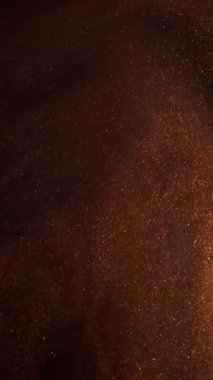 Dikey video. Parlak toz. Duman sıçrıyor. Mürekkep suyu. Bulanık kahverengi bronz altın rengi sis ışıl ışıl parçacıklar koyu siyah soyut sanat arka planında boya akışı.