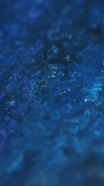 Dikey video. Parlak sıvı. Parlak mürekkep döküldü. Odaklanmamış mavi renk ışıl ışıl tanecikler akrilik boya akışkan su pigmenti karışık akış hareketi soyut sanat arka planı.