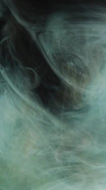 Dikey video. Uçan buhar. Duman tozu. Koyu parlak arka plan üzerinde yeşil mürekkep hareketi. Parlak, soyut fantezi sis bulutu. Parıldayan parçacıklar..