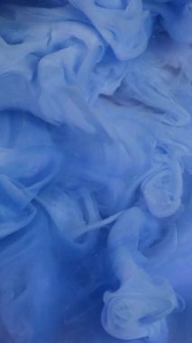 Dikey video. Mürekkep damlası. Duman bulutu. Odaklanamayan mavi renk, su altında parlayan parıldayan parıltı, sisli kütle, soyut sanat arkaplanı gibi hareket ettiğini gösteriyor..