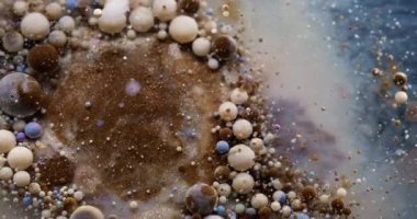 Boya akışı. Kabarcık emülsiyonu. Mistik kahverengi gri su yüzen renkli damlaları karıştırıyor. Dalgalar soyut arkaplanı doldurur.