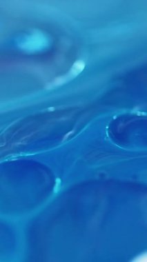 Dikey video. Yağ kabarcıkları. Köpüklü sıvı. Odaklanmamış mavi beyaz renk şeffaf yuvarlak damlacıklar yüzen jel dokusu boya su akışı hareketli soyut sanat arka planı.