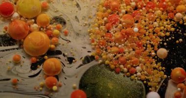 Köpüklü sıvı. Boya balonu patladı. Siyah suya dökülen parlak, yuvarlak parçacıklar. Turuncu damla pigmenti patlayan soyut arkaplan.