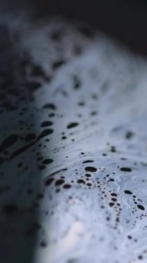 Dikey video. Asit köpüğü. Kimyasal sıvı. Odaklanmamış mavi renk baloncukları dokusu, emülsiyon, koyu siyah soyut sanat arka planında akış dalgası hareketi.