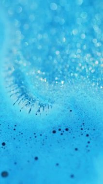 Dikey video. Islak sim dökülmüş. Bokeh ışığı. Odaklanmamış mavi renk parıldayan partiküller köpük desen akrilik boya akışı hareket soyut sanat arka planı.