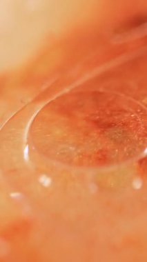 Dikey video. Serum köpükleri. Yağ sıvısı. Odaklanmamış turuncu renk şeffaf parıltılı sim desen boya su damlacıkları yüzen hareket soyut sanat arka planı.