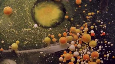 Boya damlası. Mürekkep çözülüyor. Yağlı boya damlaları koyu suda patlıyor. Sarı turuncu pigment tozu soyut sanat arkaplanı sıçratır.