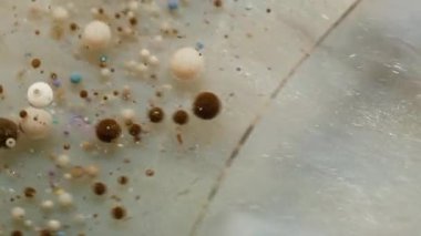 Pırıl pırıl. Kabarcık boyası. Parıldayan gümüş akıntısı akrilik damlaları karıştırıyor. Soyut beyaz bej kahverengi parçacıklar su arkaplanı.