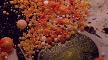 Mürekkep çözülüyor. Boya balonu patladı. Siyah suya dökülen parlak, yuvarlak parçacıklar. Turuncu damla pigmenti patlayan soyut arkaplan.