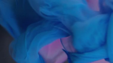 Dikey video. Sis dalgası. Suluboya kokusu. Mavi ipek pürüzsüz kıvrımlı boya cam üzerinde yüzüyor. Pembe kristal elmas. Su, soyut arkaplandan çıkarılmış..