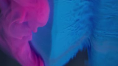Dikey video. Mürekkep akıyor. Sis boyası. Mavi elmasa damlayan pembe dalga duman parçacıkları. Bulutların soyut çözünürlüğü bulanık arkaplan.