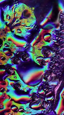 Dikey video. Akan damlalar. Islak yüzey. Yanardöner camların üzerindeki renkli akarsular. Suyun spektrum ışığı kaotik işaret fişeği parlayan nem oyunuyla yansımaları değiştiriyor.