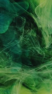 Dikey video. Gece sisi. Boya sıçraması. Yeşil sarı renkli mürekkep damlası duman bulutu koyu siyah soyut sanat arkaplanındaki yıldızı ortaya çıkarıyor.