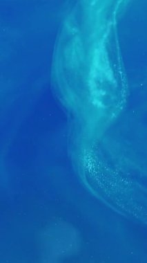 Dikey video. Parlak resim. Parıltı yanıp sönüyor. Odaklanamayan parlak mavi, soyut modern sanat arka planında ilerleyen mürekkep dumanı bulutu serpti.