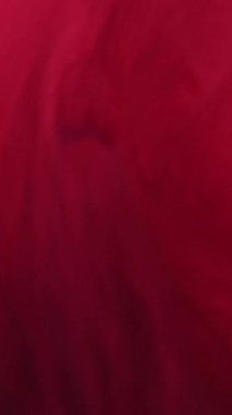 Dikey video. Renk kaybı. Mürekkep fırıl fırıl dönüyor. Odaklanamayan kırmızı parıldayan parlak duman bulutu soyut sanat arka planında parlayan sıvı damlalar..