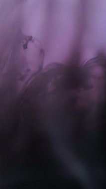 Dikey video. Su sıçramasını boya. Mürekkep damlası. Siyah mor renk boya lekeli sıvı parlak akış dumanı ışık soyut sanat arka planına yayılıyor..