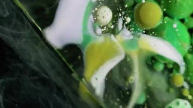 Akrilik kütle. Köpüklü sıvı. Renkli sıvı karıştırıcı köpük patlıyor. Dalgalı akan sarı yeşil beyaz parçacıklar siyah soyut arkaplan.