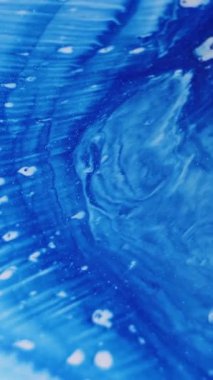 Dikey video. Mavi dökülmüş. Boya genişlemesi. Beyaz ıslak arka plan yüzeyine yayılan parlak mermer sıvı. Pürüzsüz sprey sıçrama emülsiyonu.