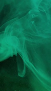 Dikey video. Sanat sıvısı. Duman girdabı. Parlayan yeşil turkuaz peçe mürekkep spreyi çözülmüş karışım parıldayan kum yüzeyi soyut su karışımı.