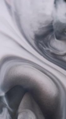Dikey video. Mürekkep çözülüyor. Grunge akışı. Gri mermer sıvı, beyaz, nemli, soyut arka plan yüzeyine yayılır. Monokrom siyah sızıntıya odaklanmış..