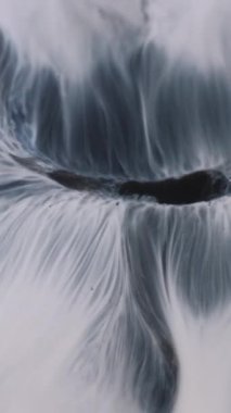 Dikey video. Sanat sıvısı. Boya pigmenti. Merkezi deliğe beyaz gri akış sızıntısı. Kirli kirli kara dalga soyut arkaplanı örtüyor.