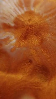 Dikey video. Boya çiçeği. Parıltı patlaması. Bakır turuncu hipnotik mermiler beyaz parlak lekeler, soyut ıslak yüzey arka planı..