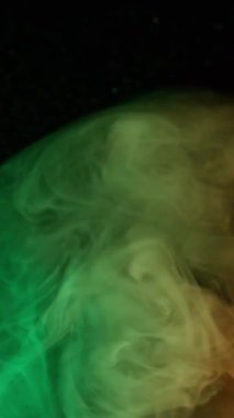 Dikey video. Renkli duman. Mistik akış. Duman mürekkebi patlaması pırıl pırıl parlayan yüzeye yayılan kıvrımlar siyah soyut parlak bulanık su arkaplanı.