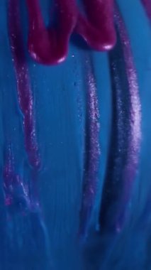 Dikey video. Parıltı dökülüyor. Boya damlaları. Mor parıldayan akryl akıntıları mavi küreye dökülüyor. Sanat arkaplan akışı cilası su soyut sıvısını bulanıklaştırır.