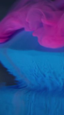 Dikey video. Mürekkep akıyor. Sis boyası. Mavi elmasa damlayan pembe dalga duman parçacıkları. Bulutların soyut çözünürlüğü bulanık arkaplan.