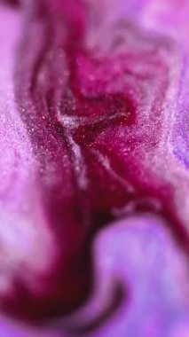 Dikey video. Işıldayan sıvı dökülmesi. Islak sim akışı. Odaklanmamış morumsu pembe renkli parlak parçacıklar akrilik mürekkep dalgası, soyut sanat arkaplanı ve bokeh ışık.