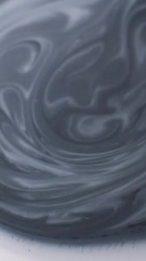 Dikey video. Grunge akışı. Boya genişlemesi. Gri siyah mermer sıvı, beyaz, ıslak, soyut arka plan yüzeyine yayılır. Tek renk çözünmüş serpinti..