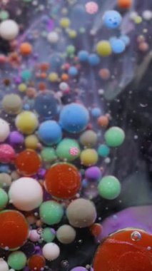 Dikey video. Baloncuk döküldü. Mürekkep akışı. Yağlı boya damlaları suda eriyor. Renkli akrilik pigment köpük yüzen soyut sanat arkaplanı.