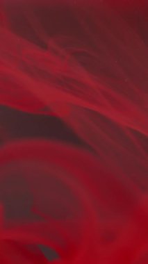 Dikey video. Mürekkep suyu üflüyor. Bulanık duman boyası. Odaklanmamış kırmızı renk parlatıcı sıvı damlalar akış sıvısı buhar doku dalgası soyut sanat koyu arkaplan üzerinde.