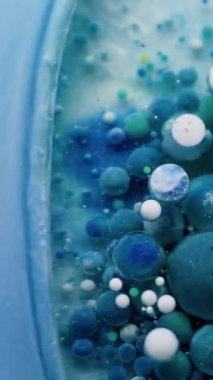 Dikey video. Yağ damlası. Boya karışımı. Şeffaf yuvarlak su yüzeyinde yüzen renkli jel damlaları. Fantezi mavisi soyut sıvı arkaplan.